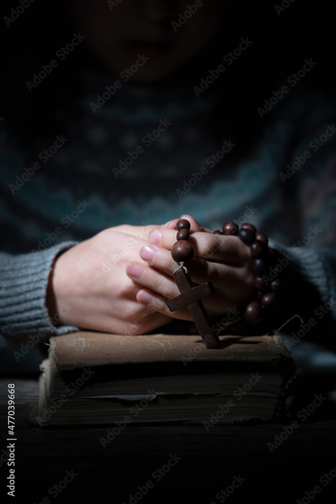 Portrait of young beautiful girl praying to God with rosary.