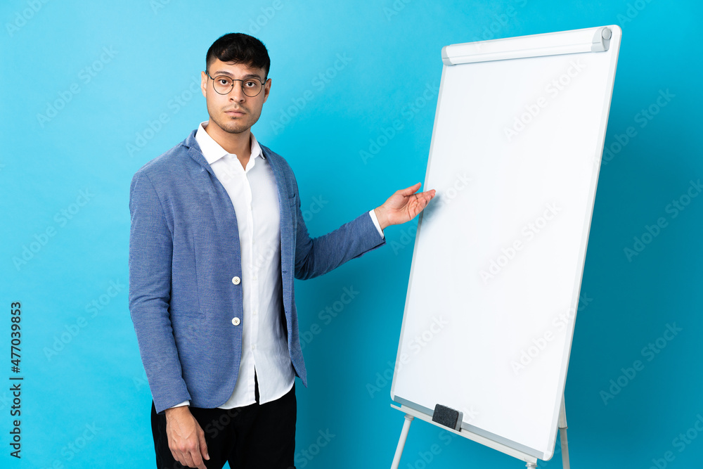 Young Colombian man isolated on blue background giving a presentation on white board Young Colombian man isolated on blue background giving a presentation on white board