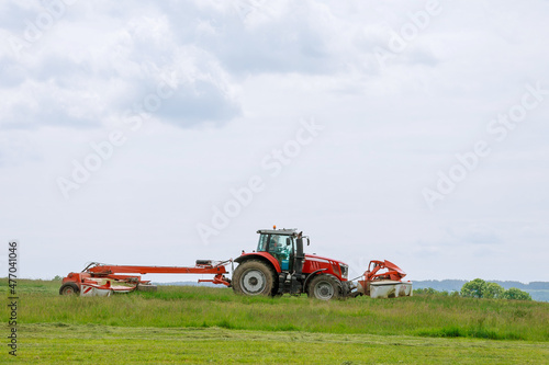 A red tractor mows the grass on a farmer s field. Two mowers will mow a large area of the field.