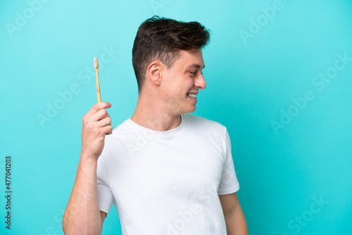 Young Brazilian man brushing teeth isolated on blue background looking side