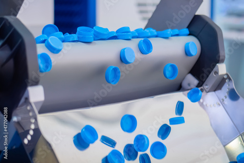 Many blue plastic bottle caps falling from conveyor belt at factory, exhibition - production line. Manufacturing, recycling, industry, technology equipment concept