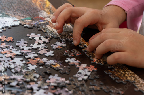 Little girl doing jigsaw puzzle at home. Close up photo with selective focus.