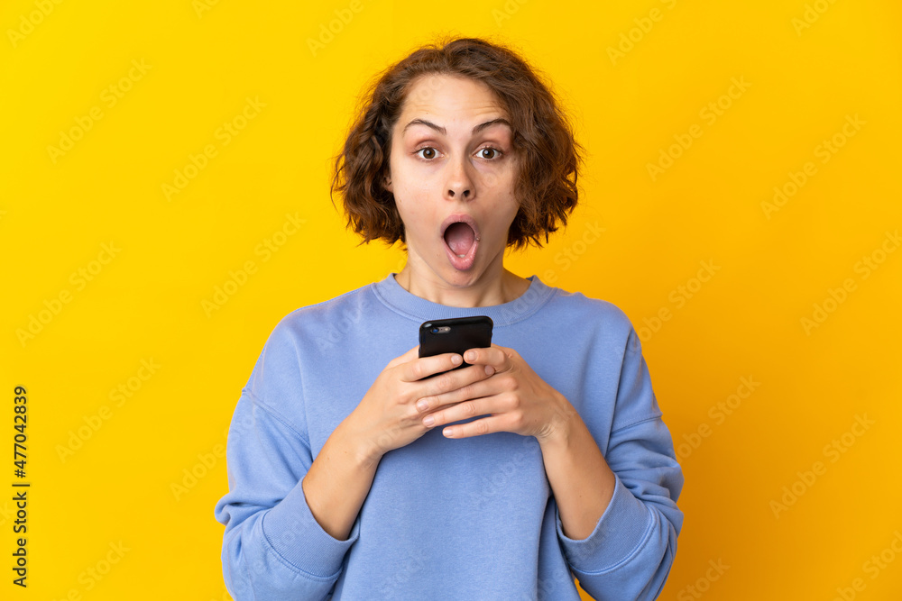 Young English woman isolated on pink background looking at the camera while using the mobile with surprised expression
