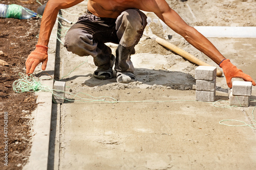 A young bare-chested worker uses nylon string to level paving slabs on a bright sunny day.