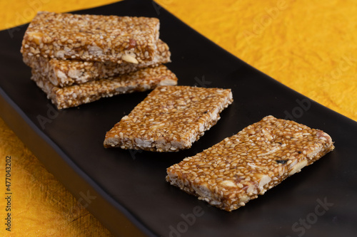 Sweet Mithai on yellow background for Makar Sankranti Lohri Gajak Also Known As Gur Gajjak Gazak Gachak Til Patti Papdi Chikki Made Of til or sesame seed Jaggery Gud Almonds Badam And Pistachio