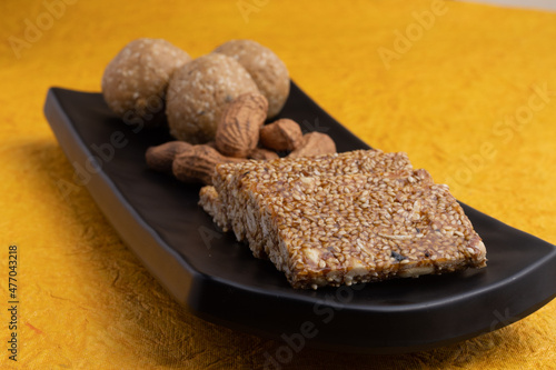 Traditional sweet Mithai for Makar Sankranti Lohri Gajak Also Known As Gur Gajjak Gazak Gachak Til Patti Papdi Chikki Made Of til sesame seed Jaggery Gud Almond Badam Pistachion on yellow background photo