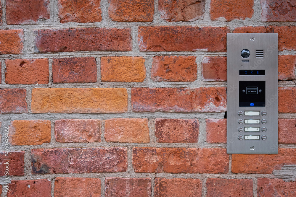 Video intercom on red brick wall background. Modern, luxury, wealthy home security system. Alarm door bell. Safe entrance to the apartment. Smart home technology, street view. Close up, copy space