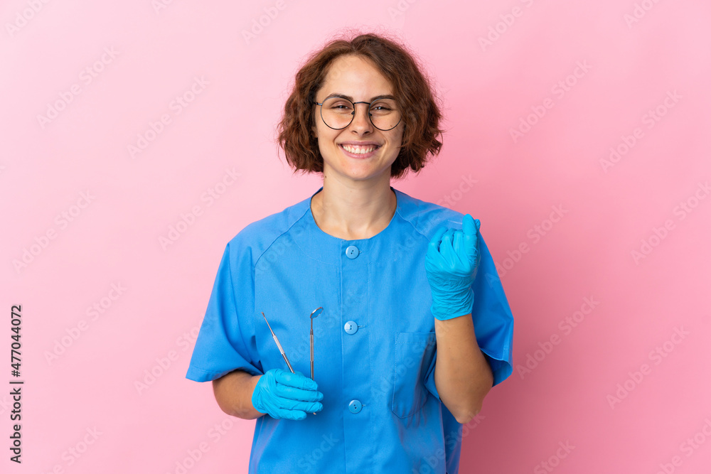 Woman English dentist holding tools over isolated on pink background making money gesture Woman English dentist holding tools over isolated on pink background making money gesture