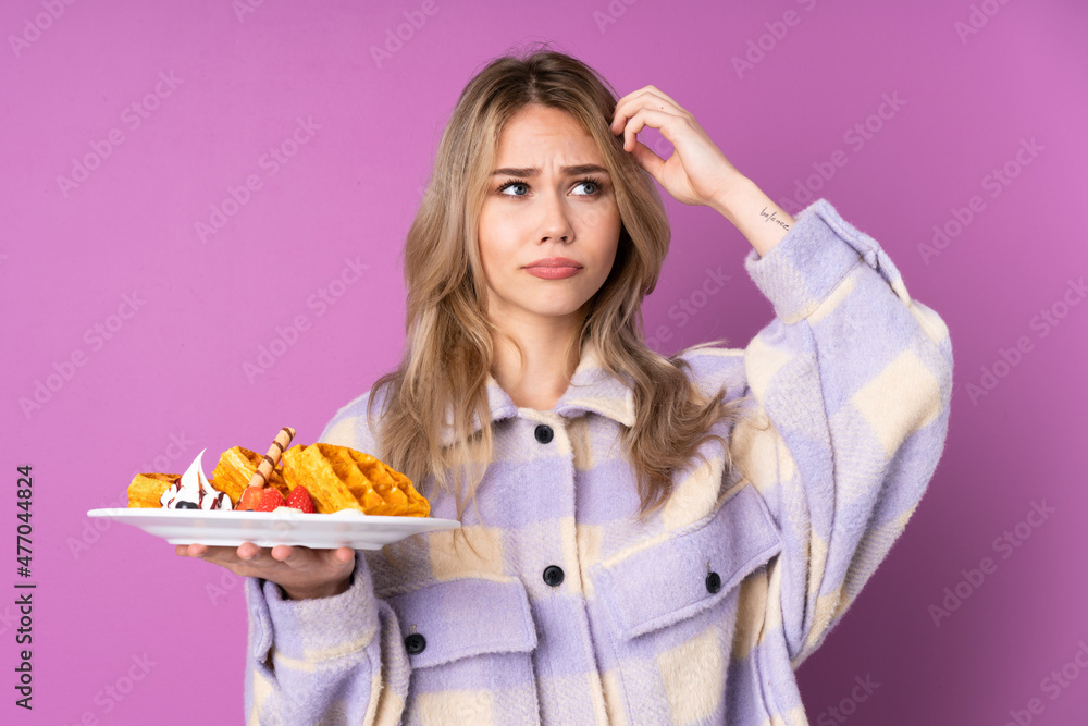Teenager Russian girl holding waffles isolated on purple background having doubts while scratching head Teenager Russian girl holding waffles isolated on purple background having doubts while scratching head