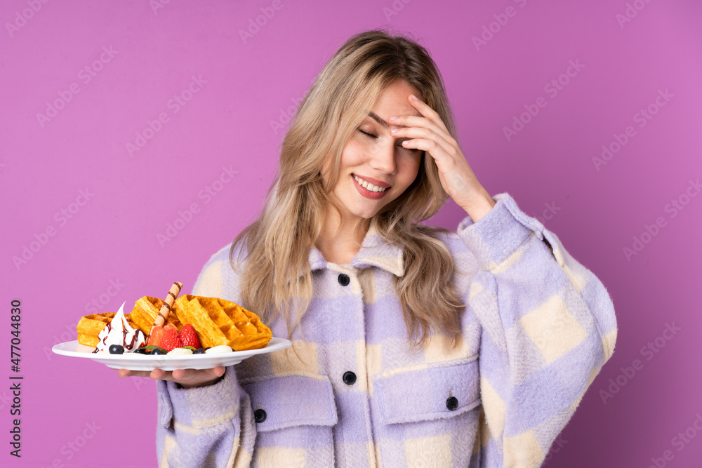 Teenager Russian girl holding waffles isolated on purple background laughing Teenager Russian girl holding waffles isolated on purple background laughing