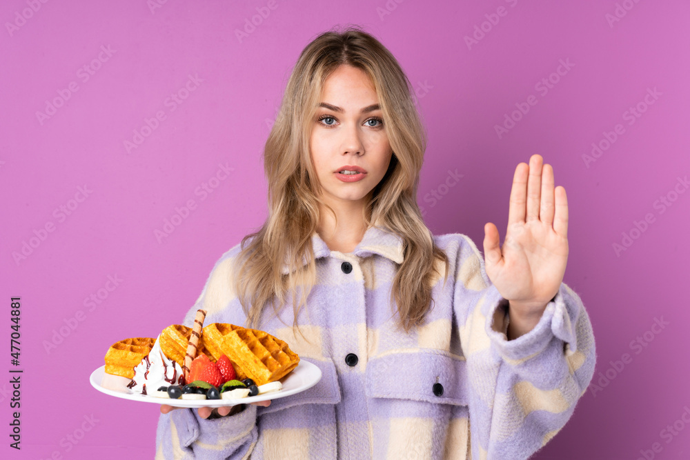 Teenager Russian girl holding waffles isolated on purple background making stop gesture and disappointed Teenager Russian girl holding waffles isolated on purple background making stop gesture and disappointed