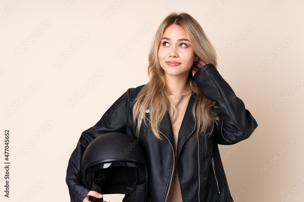 Russian girl with a motorcycle helmet isolated on beige background thinking an idea Russian girl with a motorcycle helmet isolated on beige background thinking an idea