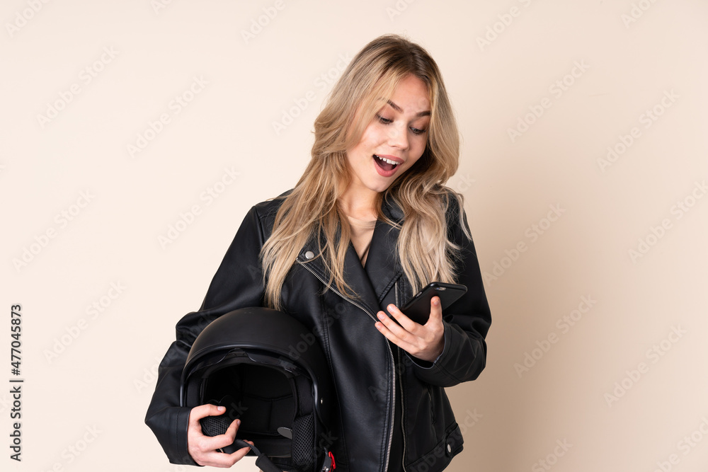 Russian girl with a motorcycle helmet isolated on beige background surprised and sending a message Russian girl with a motorcycle helmet isolated on beige background surprised and sending a message