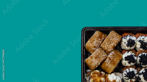 Sushi roll set in a plastic container. An isolated set dries on Color Hex Teal. Top view. Container with fresh sushi at the bottom right. Sushi with smoked eel and caviar.
