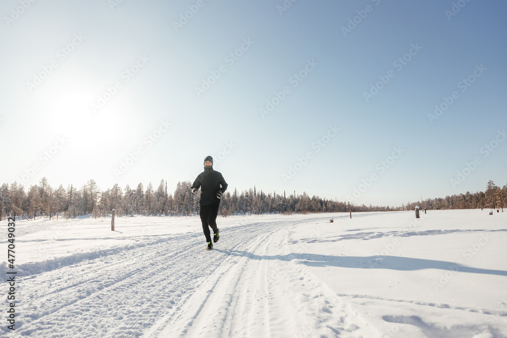 Full length of a happy middle-aged athlete running in nature on a snowy winter day. Outdoor fitness, cardio training, outdoor exercises