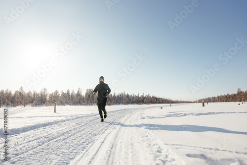 Full length of a happy middle-aged athlete running in nature on a snowy winter day. Outdoor fitness, cardio training, outdoor exercises