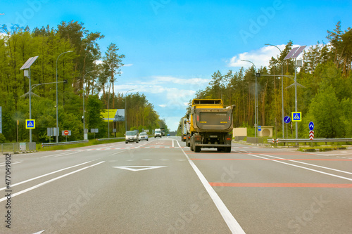 Kiev  Ukraine. May 5  2021. Cars moving on a paved highway road in the forest  wood with green trees against blue sky at sunny summer or spring day. Truck  cars in motion. Transport  transportation.