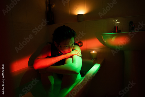 Young sad depressed woman hugging knees sitting in clothes in bathtub under neon light, feeling lonely or having breakup depression, suffering from mental problems. Anxiety after ending relationship photo