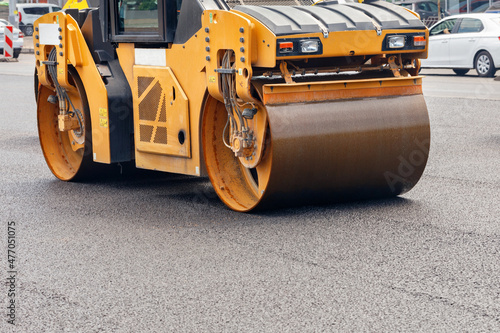 A road roller compacts fresh asphalt on the roadway on a city street.