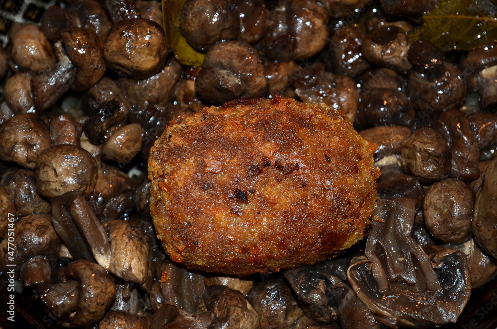 The meat cutlet lies on champignon mushrooms.