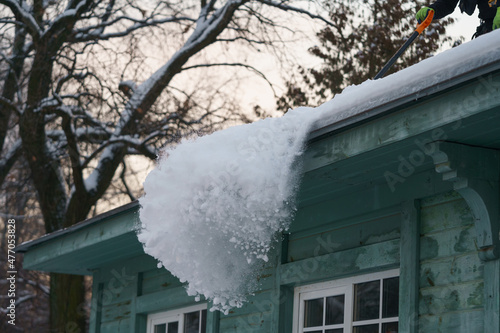 Obraz na plátně Cropped photo of man homeowner removing clearing snow from edge of roof on winter day, qualified professional holding shovel cleaning rooftop from ice and icicles during wintertime