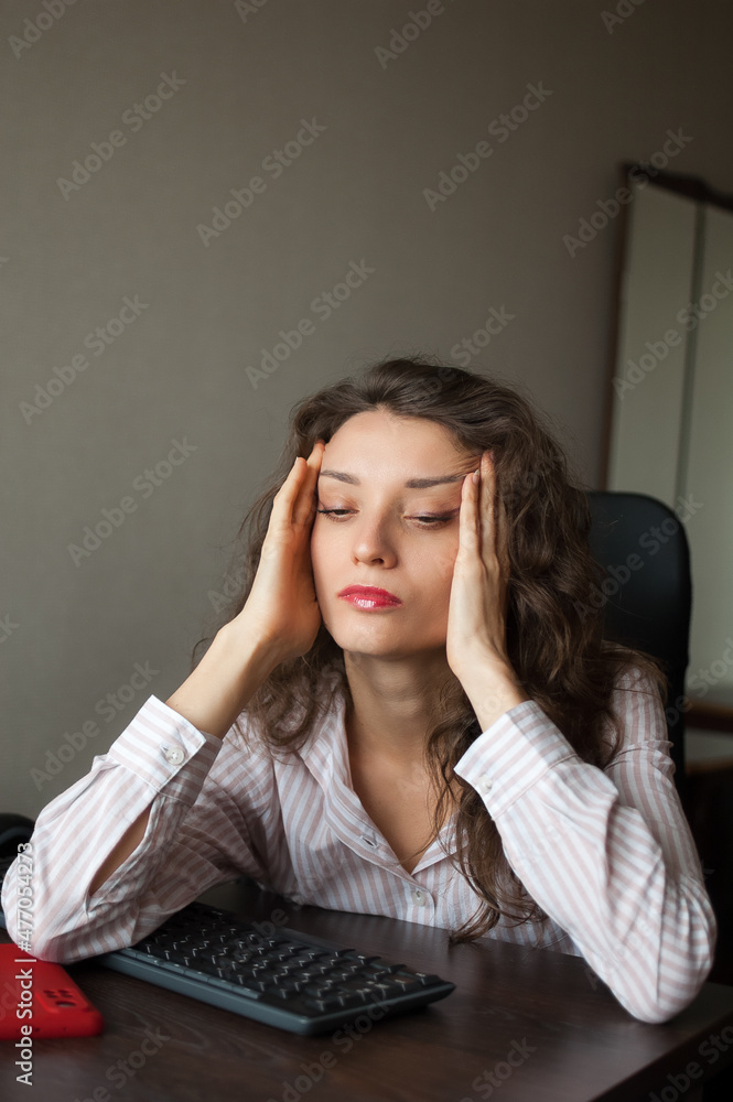 Tired young woman with curly hair and white shirt is working at the office using her laptop, routine work, freelance, burnout syndrome Tired young woman with curly hair and white shirt is working at the office using her laptop, routine work, freelance, burnout syndrome