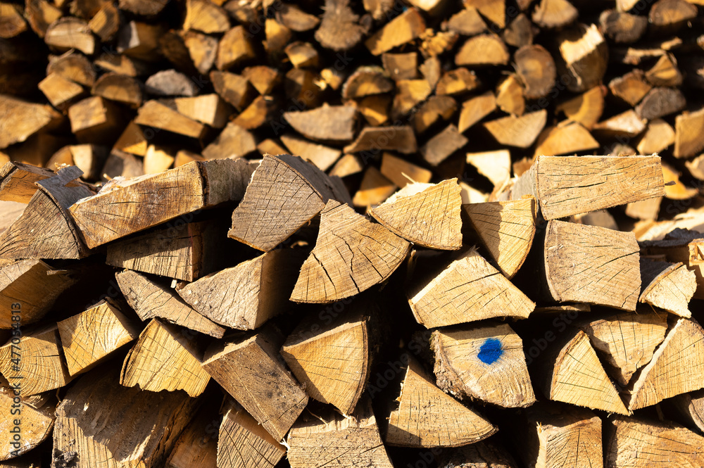 Vorne flacher Holzstapel im Fokus und im Hintergrund hoher Holzstapel aus gehacktem und ordentlich aufgeschichtetem Scheitholz und Kleinholz zum Trocknen für Kaminholz und Brennholz