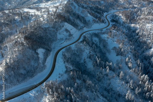 The highway passes through the pass in winter, top view of the snowy forest in winter. Snow-covered road runs through the forest in the mountains through the pass in December.