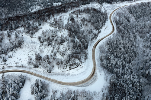 The highway passes through the pass in winter, top view of the snowy forest in winter. Snow-covered road runs through the forest in the mountains through the pass in December. © ezumer