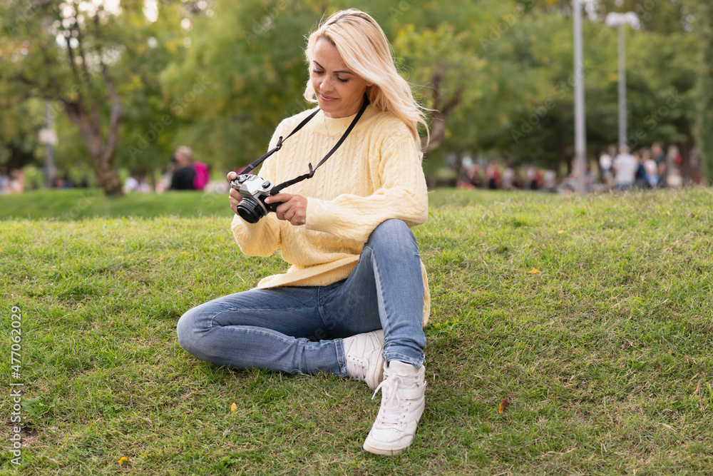 Fototapeta premium Blonde woman sitting on a park while using a camera