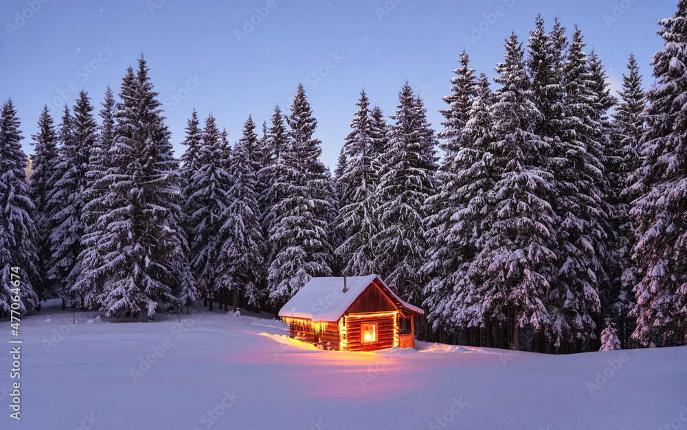 The lamps light up the house at the evening time. Winter landscape. Wooden hut on the lawn covered with snow. Mystical night. Marry Christmas and New Year. Mountains and forests. Wallpaper background.