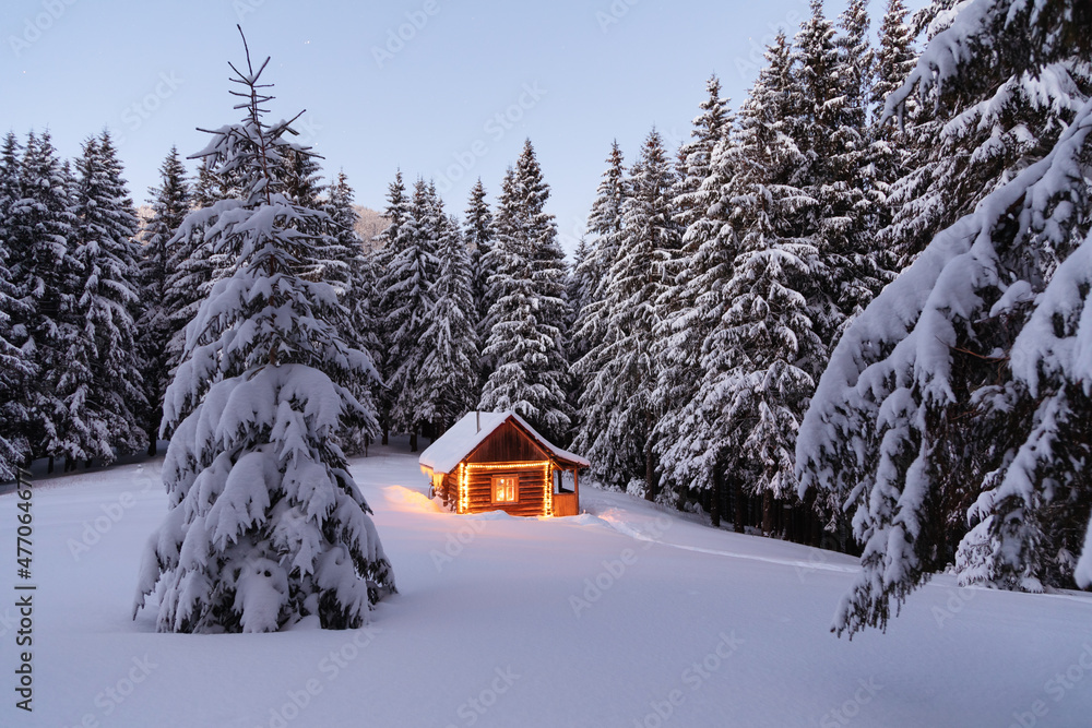 The lamps light up the house at the evening time. Winter landscape. Wooden hut on the lawn covered with snow. Mystical night. Marry Christmas and New Year. Mountains and forests. Wallpaper background.