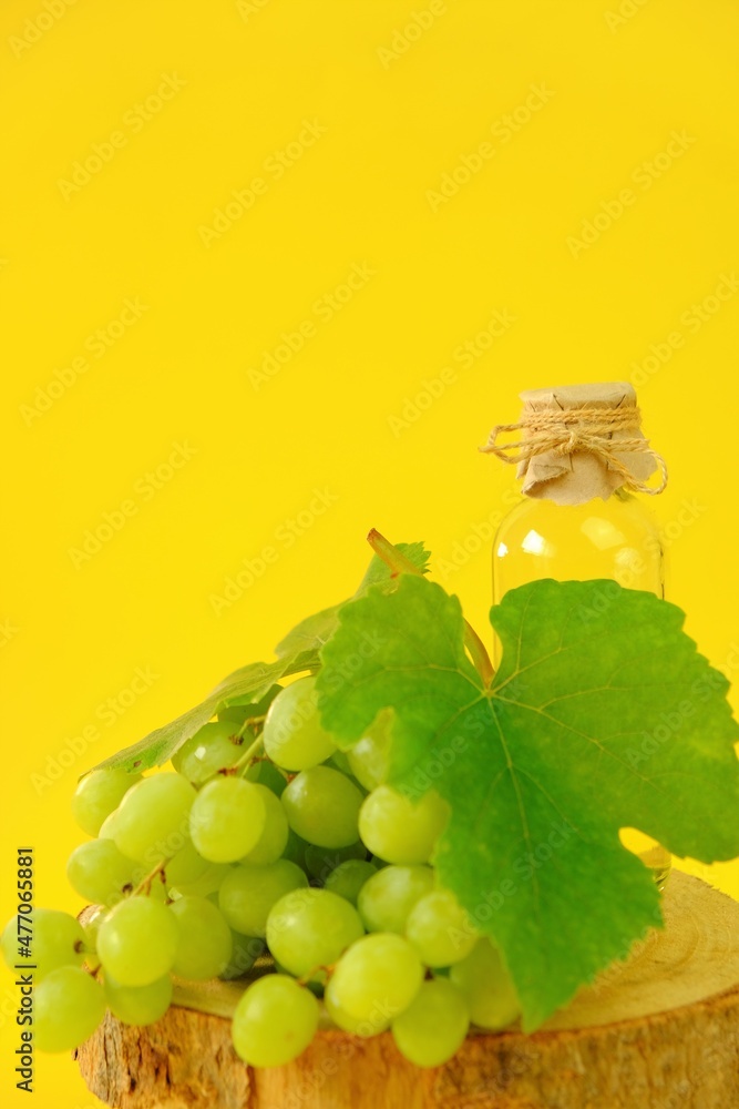 Grape seed oil.Base cosmetic oil for massage and care for face and body. bottle and bunch of green grapes on a bright yellow background.