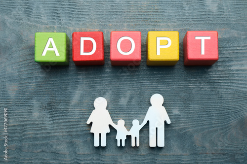 Family figure and word Adopt made of cubes on blue wooden table, flat lay photo