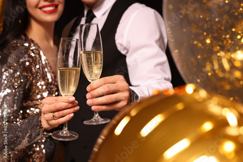 Couple with glasses of sparkling wine celebrating New Year on black background, closeup photo