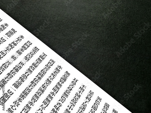 横長の黒いコピースペースの手前斜めに『般若心経』の一部が書かれた白い紙。仏教、宗教、東洋のイメージ素材。