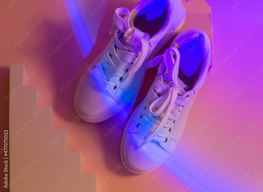 Trendy fashion white sneakers on geometry podium on abstract bright background. Neon lights on casual shoes. Violet and orange gradient light. Minimalism 90s 80s concept. Stock Photo Adobe Stock