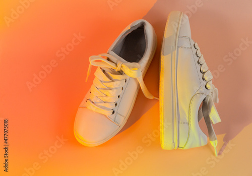 Trendy fashion white sneakers on abstract bright background. Neon lights on casual shoes. Orange and red gradient light. Minimalism, 90s concept.