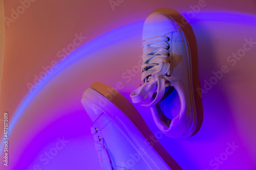 Trendy fashion white sneakers on abstract bright background. Neon lights on casual shoes. Orange and violet gradient light. Minimalism, 90s concept.