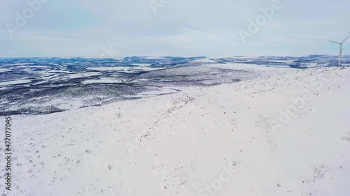 Aerial view of a mountain and arctic wilderness with windmills, winter in Enontekio, Finland - reverse, tilt, drone shot photo