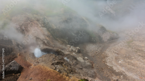Geyser erupts on the hillside. A fountain of boiling water rises up. A hot stream flows along a rocky bed in the valley of Geysers. Everything is hidden by steam and haze. Poor visibility. Kamchatka