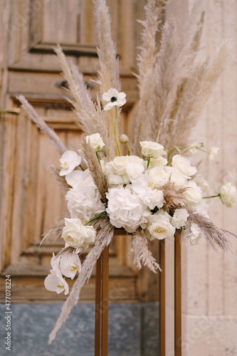 Bouquet with a cortaderia and white flowers stands on a gold pedestal in front of a wooden door photo