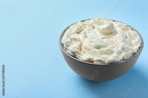 Bowl of tasty cream cheese on light blue background, space for text