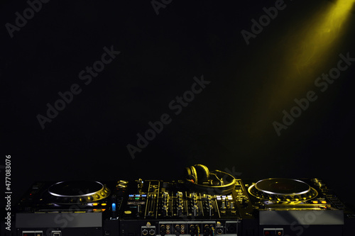 Fotografie Modern DJ controller and headphones under beam of light on black background