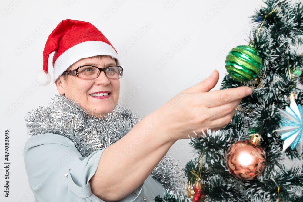 An elderly woman decorates a Christmas tree.