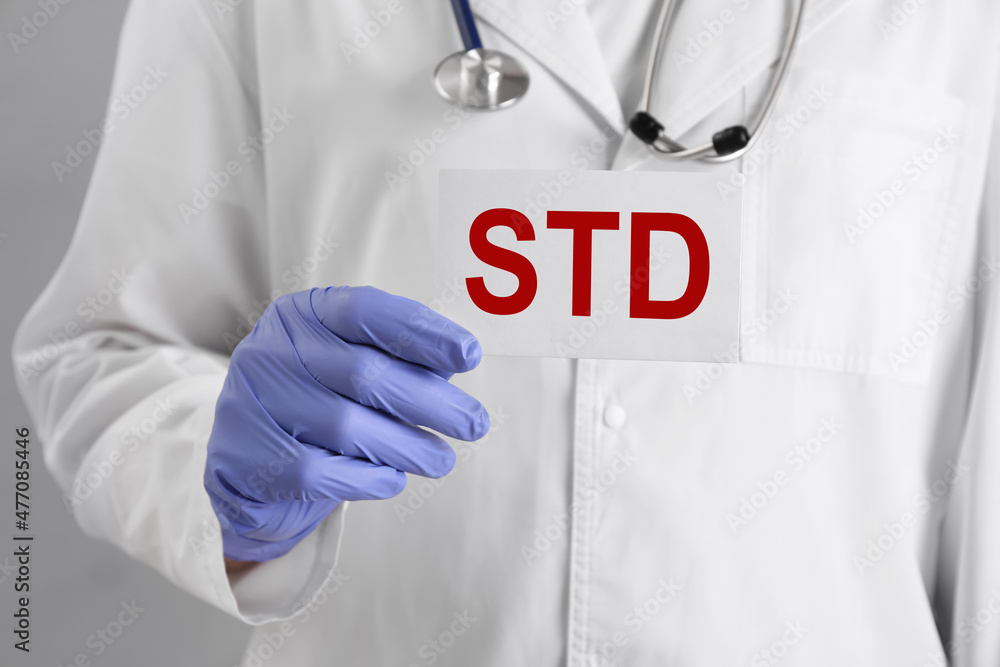 Doctor holding sheet of paper with abbreviation STD on grey background, closeup Doctor holding sheet of paper with abbreviation STD on grey background, closeup