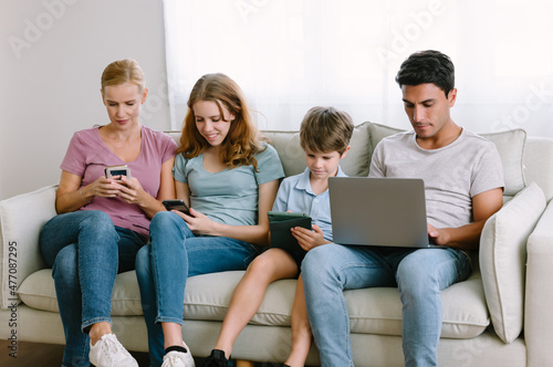 Portrait of caucasian family holding and using different electronic gadgets, spending time online, playing games, checking social network while sits on sofa in living room at home. Gadgets addiction.
