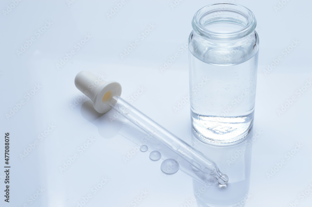 glass transparent jar and a cosmetic pipette with liquid droplets on a white background. glass transparent jar and a cosmetic pipette with liquid droplets on a white background.