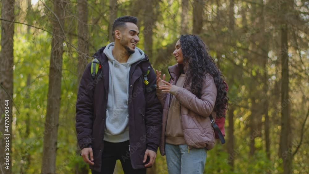 Urban people got lost in wood. Funny cheerful Multinational couple of diverse friends waving hands, showing correct route, laughing. Hispanic woman and arabic man walking having fun in autumn forest Urban people got lost in wood. Funny cheerful Multinational couple of diverse friends waving hands, showing correct route, laughing. Hispanic woman and arabic man walking having fun in autumn forest