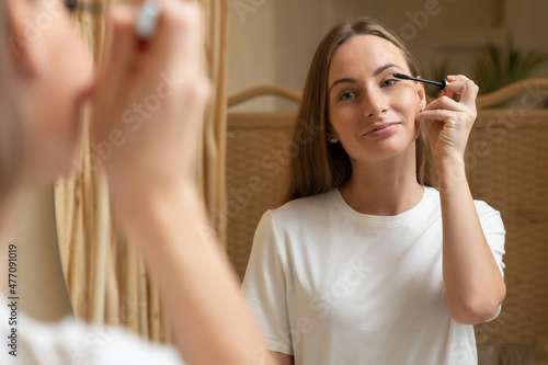 Woman using mascara on eyelash in bathroom in the morning time. Young woman applying eye make up and looking at mirror.